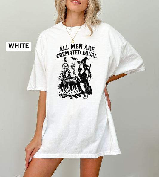 Person wearing a white graphic t-shirt with a skeleton and witch design, sitting on the ground.