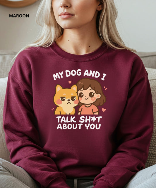 Person wearing a maroon sweatshirt with a graphic and text that says"my dog and i talk shit about you", sitting on a couch.