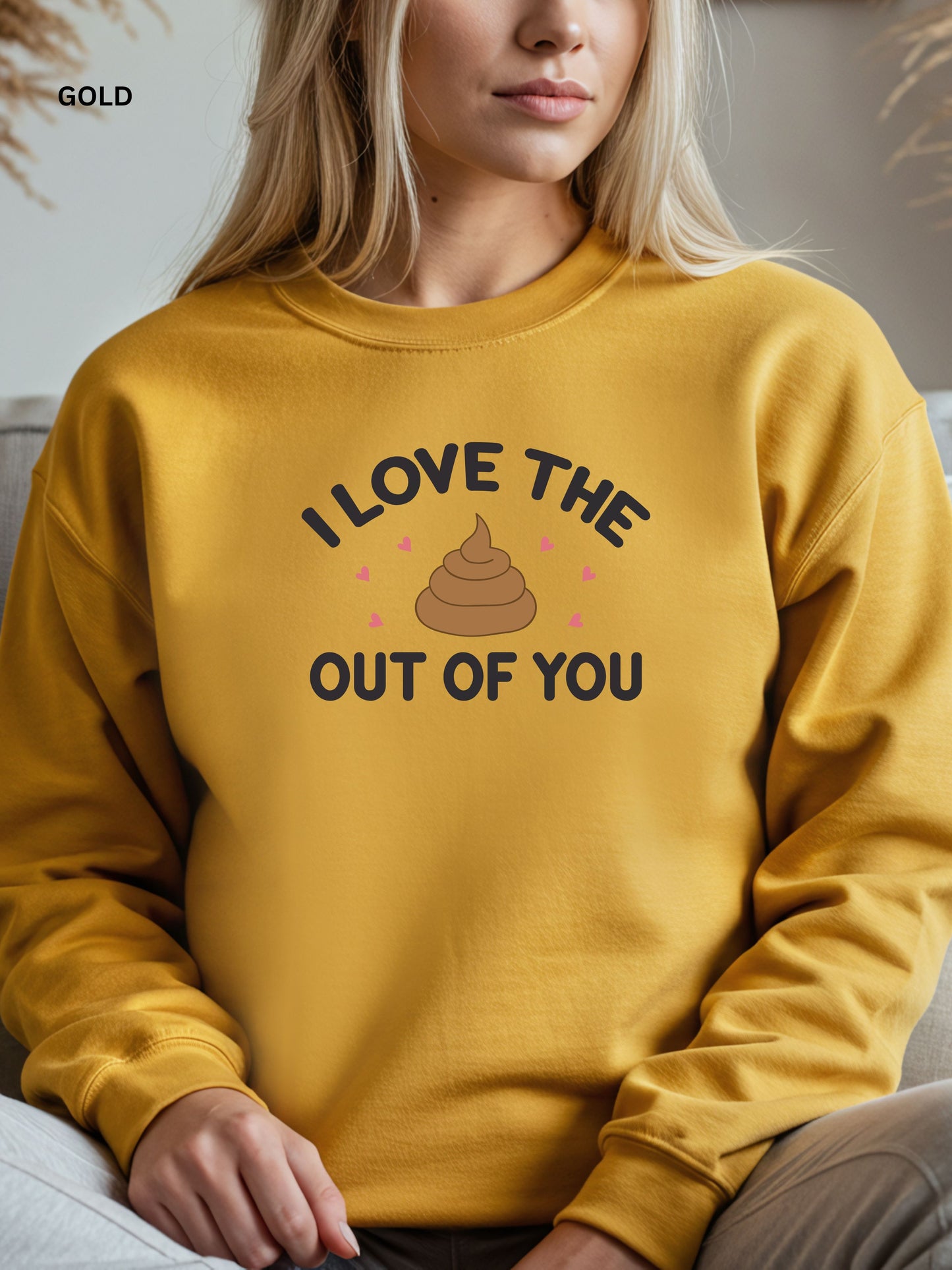 Person wearing a gold sweatshirt with a humorous design that says"i love the shit out of you", sitting on a couch.