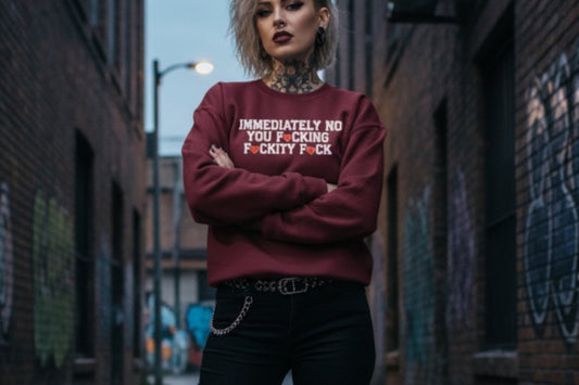 Person wearing a maroon sweatshirt with text and ripped black jeans standing in an alleyway.