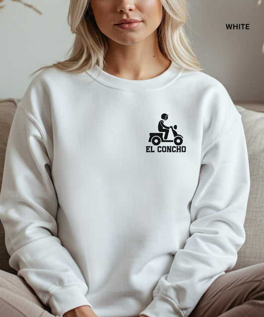 Person wearing a white sweatshirt with a logo and text that says" el concho", sitting on a couch.