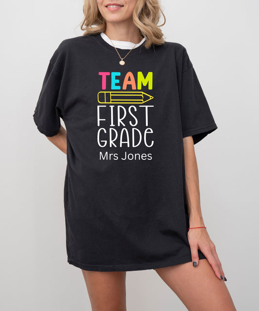Black t-shirt with 'Team First Grade Mrs Jones' text worn by a person on a plain background