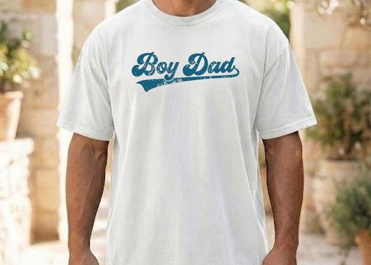 Person wearing a white t-shirt with 'Boy Dad' text in blue outdoors.