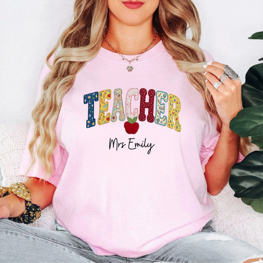 Personalized teacher shirt in Blossom with faux patchwork TEACHER lettering, red apple graphic, and custom name — garment-dyed heavyweight tee