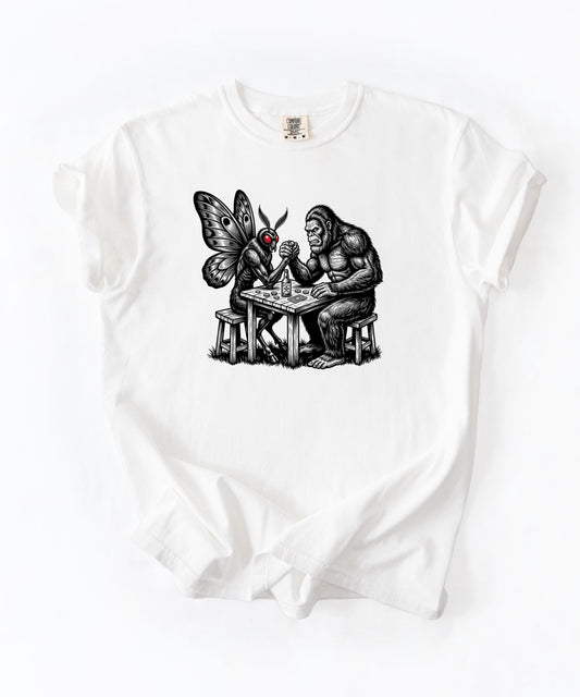 White garment-dyed unisex Bigfoot vs Mothman arm wrestling graphic tee โ funny cryptid shirt