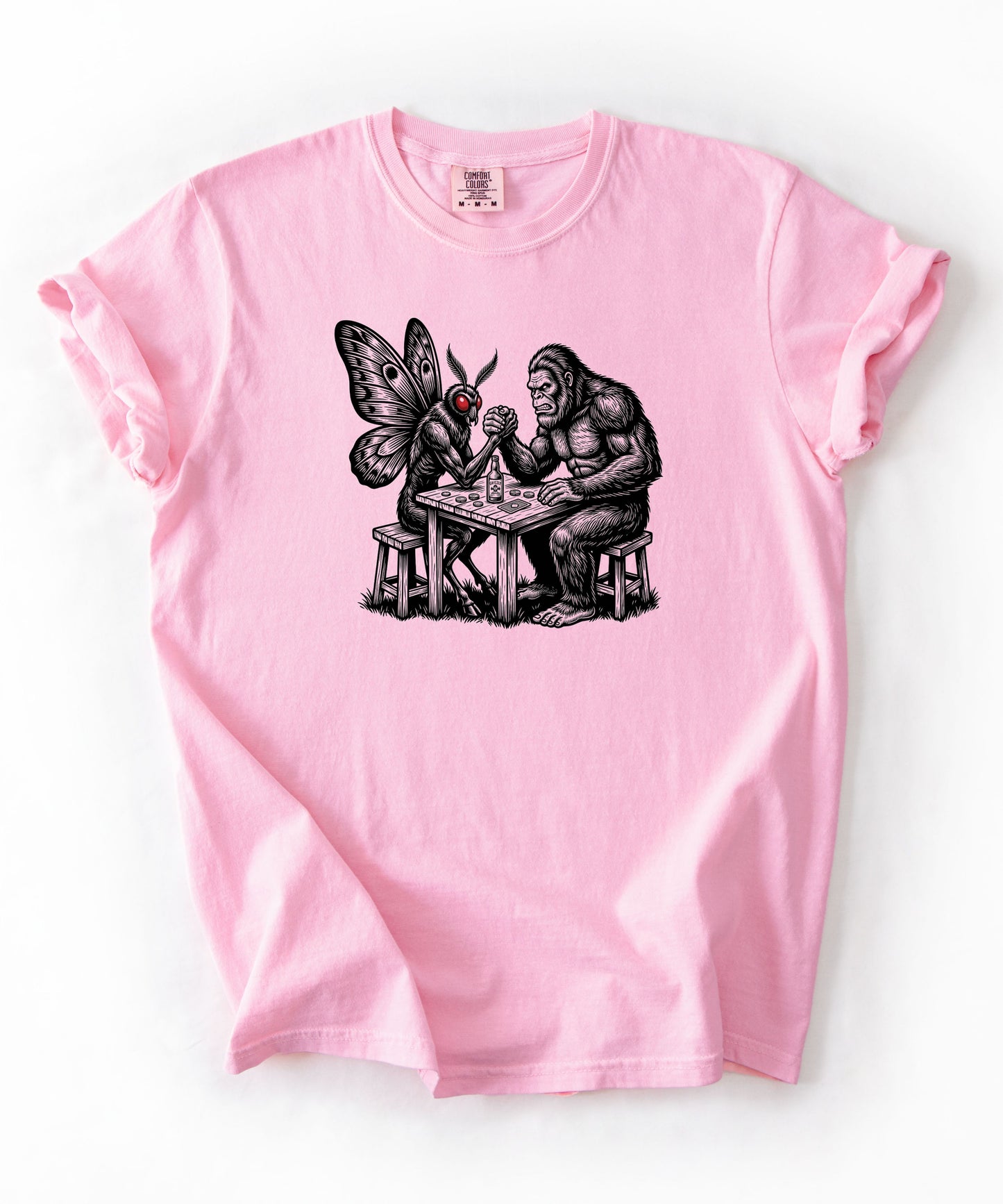 Blossom garment-dyed unisex Bigfoot vs Mothman arm wrestling graphic tee — funny cryptid shirt
