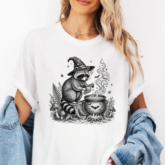Witch Raccoon Cauldron T-Shirt in White — vintage cottagecore graphic tee with hand-drawn woodland witch design