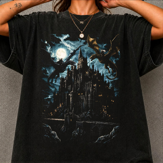 A person wearing a black graphic t-shirt featuring a dark fantasy illustration of a gothic castle under a full moon with dragons, set against a gray textured background.