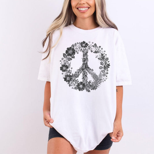 A woman wearing an oversized white t-shirt with a black floral peace sign graphic on the front, paired with black shorts, against a plain white background.