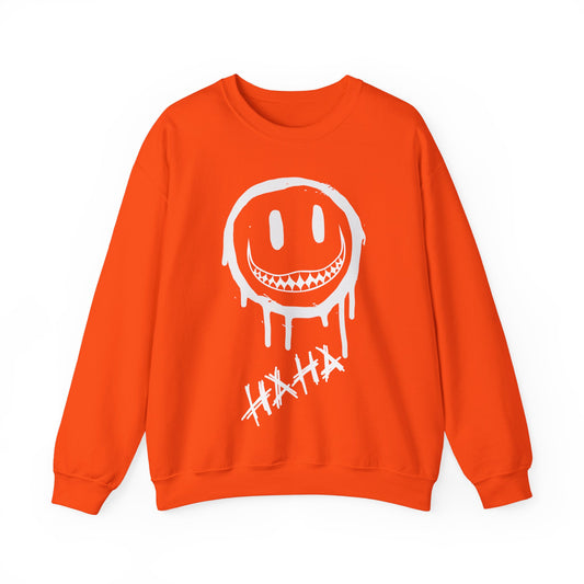 An orange crewneck sweatshirt featuring a white dripping smiley face graphic with sharp teeth and the word 'HAHA' written below it, displayed on a clean white background.
