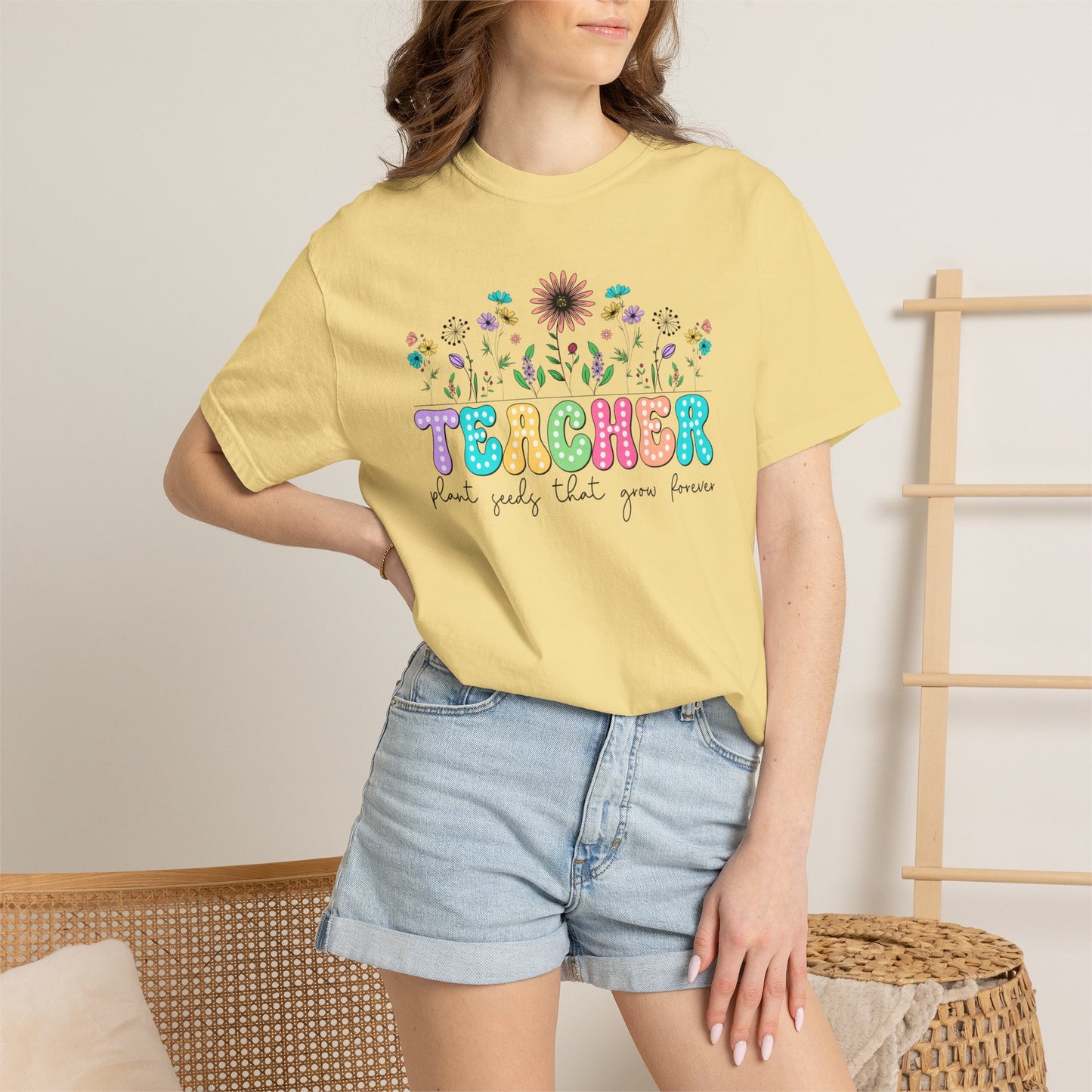 Person wearing a banana colored t-shirt with colorful 'TEACHER' design and floral elements.