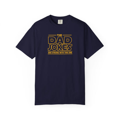 a true navy t-shirt with yellow text 'The Dad Jokes Are Strong With This One' in front of a blurred background.