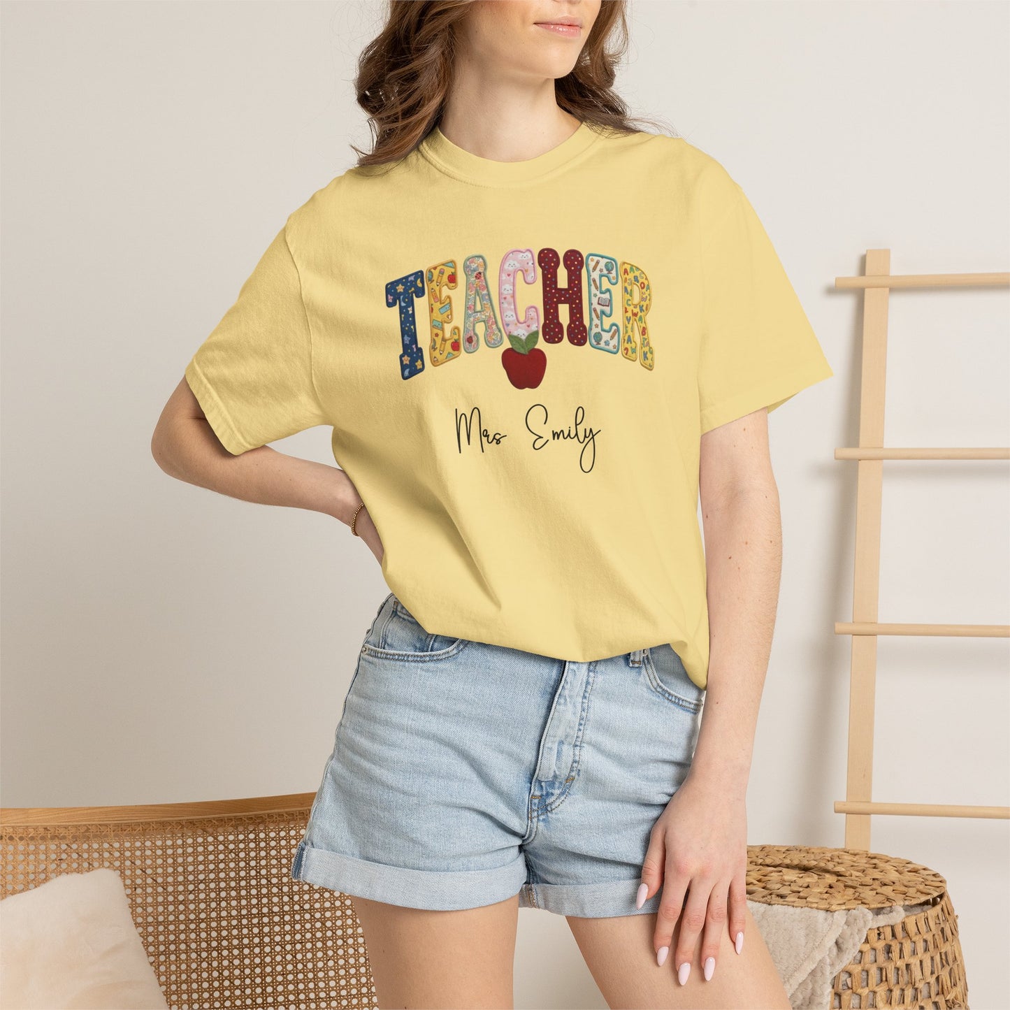 Personalized teacher shirt in Butter with faux patchwork TEACHER lettering, red apple graphic, and custom name — garment-dyed heavyweight tee
