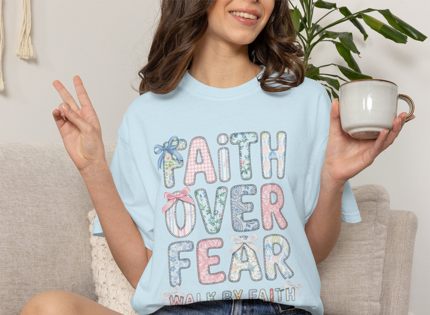 Person wearing a chambray t-shirt with 'Faith Over Fear' text, sitting on a couch holding a mug.