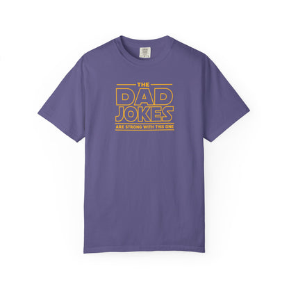 a grape t-shirt with yellow text 'The Dad Jokes Are Strong With This One' in front of a blurred background.