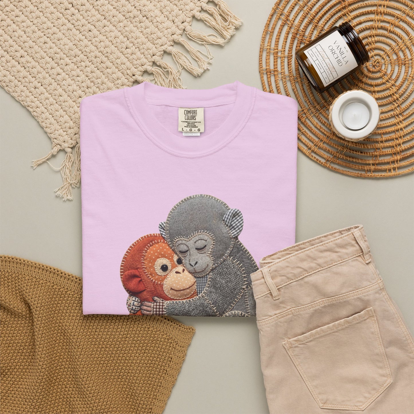 Folded orchid t-shirt with monkey design on a neutral surface with pants and decor items.