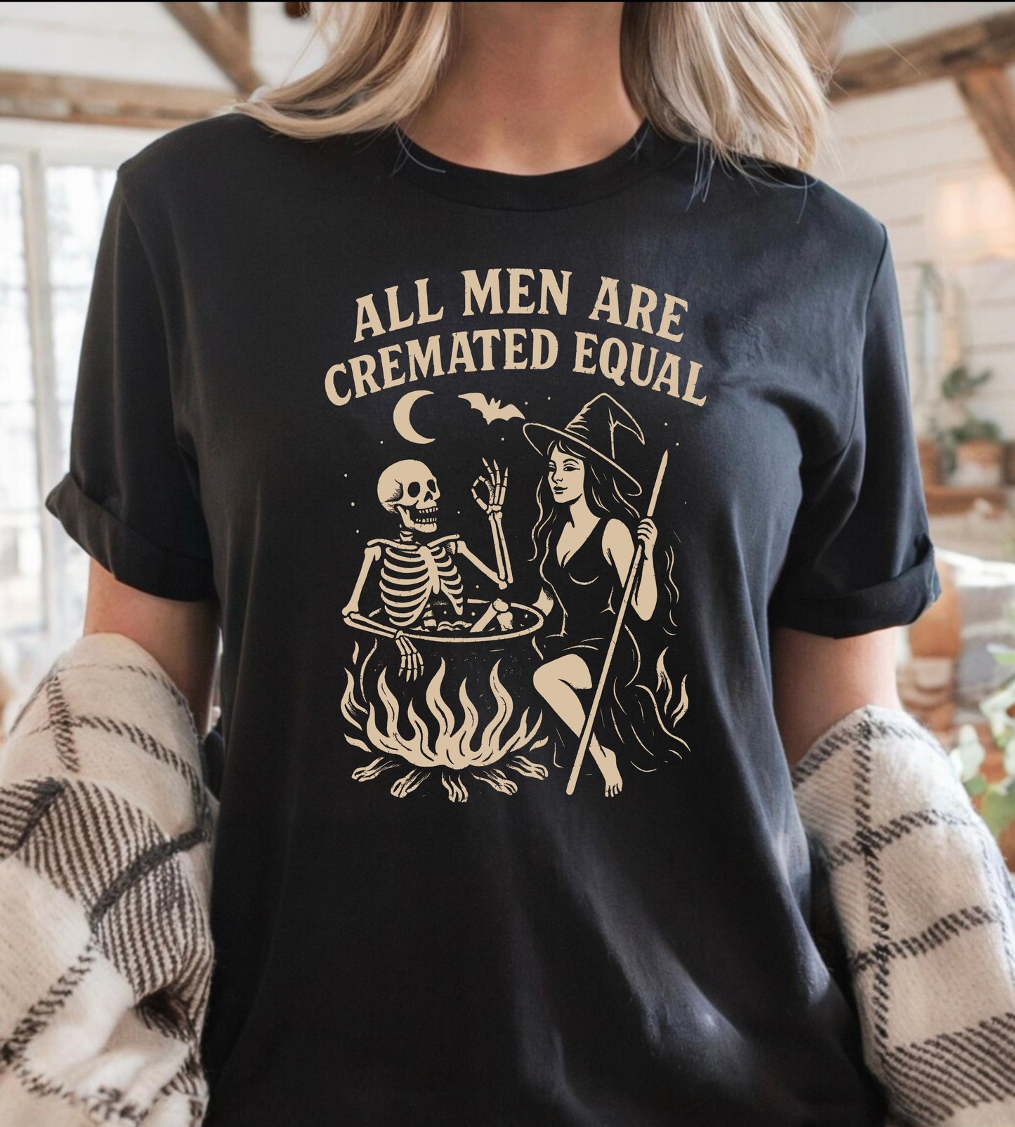 Person wearing a black graphic t-shirt with a skeleton and witch design, sitting on the ground.