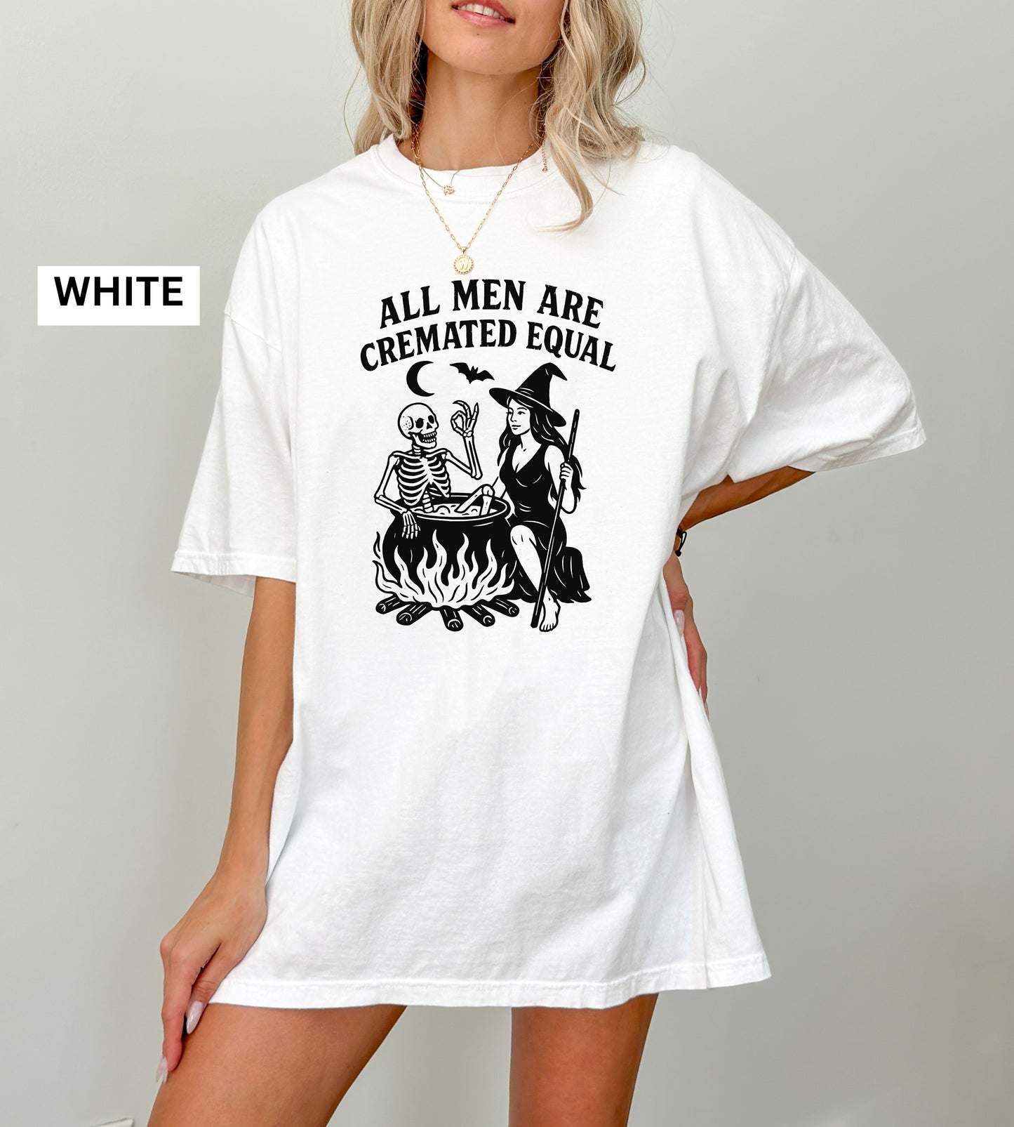 Person wearing a white graphic t-shirt with a skeleton and witch design, sitting on the ground.
