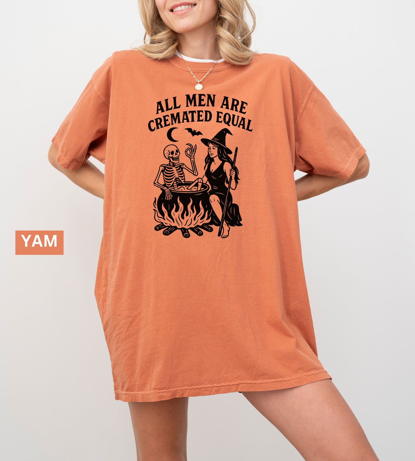 Person wearing a yam graphic t-shirt with a skeleton and witch design, sitting on the ground.