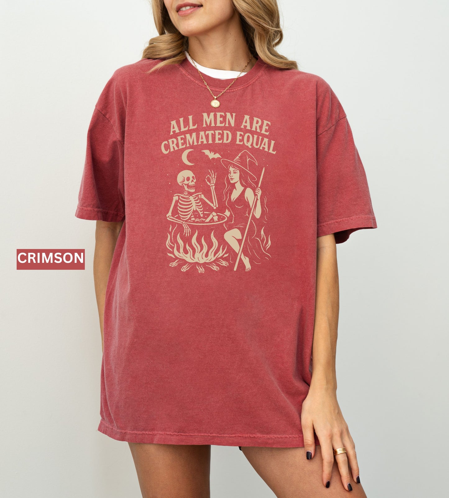 Person wearing a crimson graphic t-shirt with a skeleton and witch design, sitting on the ground.