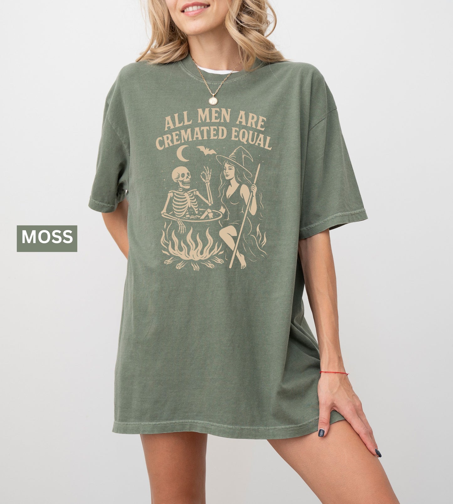 Person wearing a moss graphic t-shirt with a skeleton and witch design, sitting on the ground.