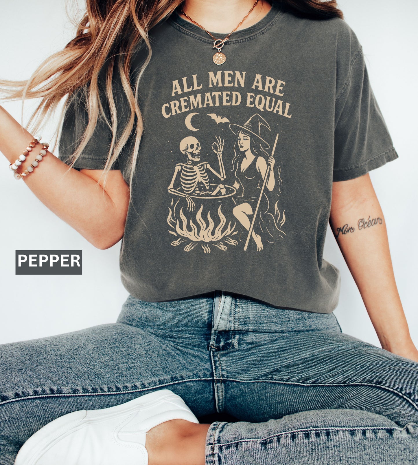 Person wearing a graphic t-shirt with a skeleton and witch design, sitting on the ground.