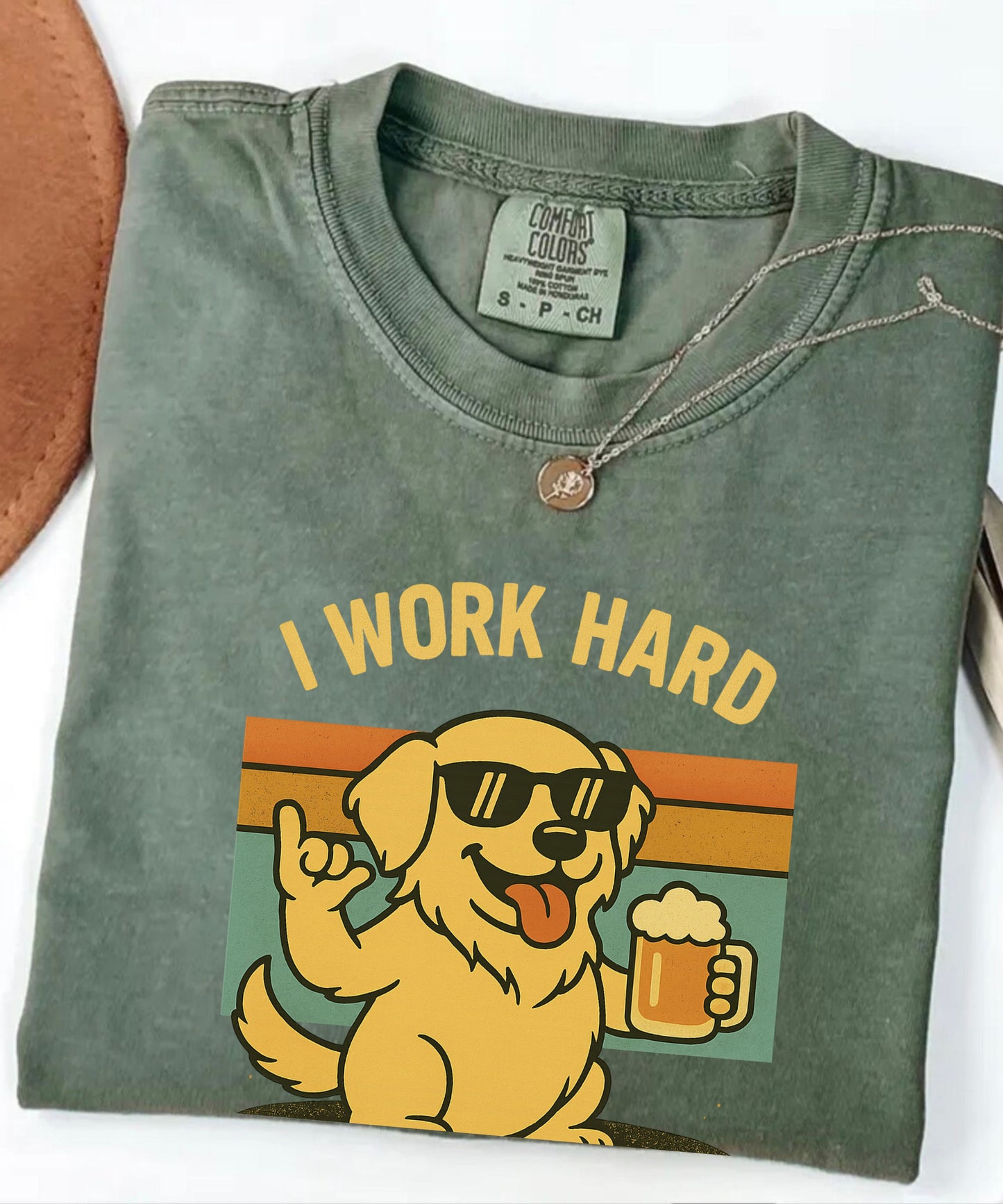 Folded green t-shirt with a dog graphic and 'I Work Hard' text on a white background