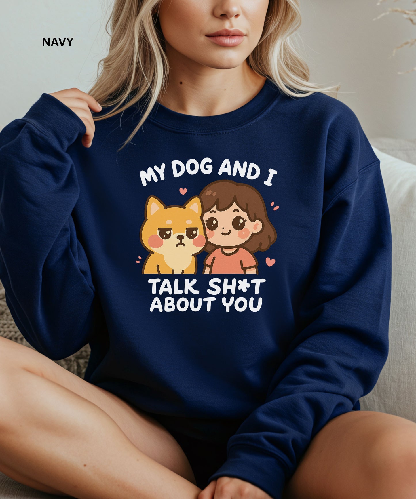 Person wearing a navy sweatshirt with a graphic and text that says"my dog and i talk shit about you", sitting on a couch.