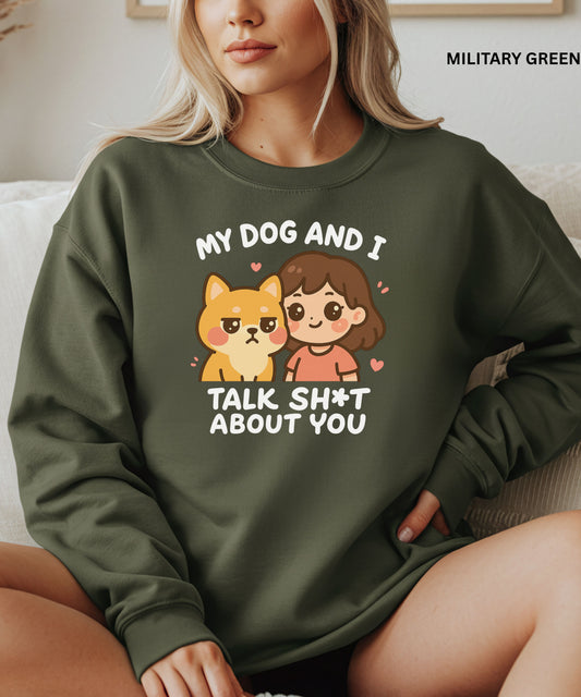 Person wearing a military green sweatshirt with a graphic and text that says"my dog and i talk shit about you", sitting on a couch.