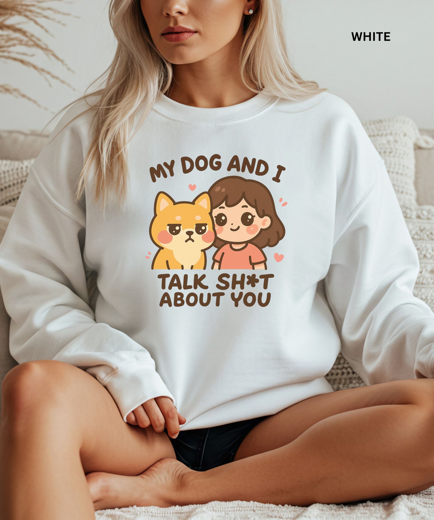 Person wearing a white sweatshirt with a graphic and text that says"my dog and i talk shit about you", sitting on a couch.