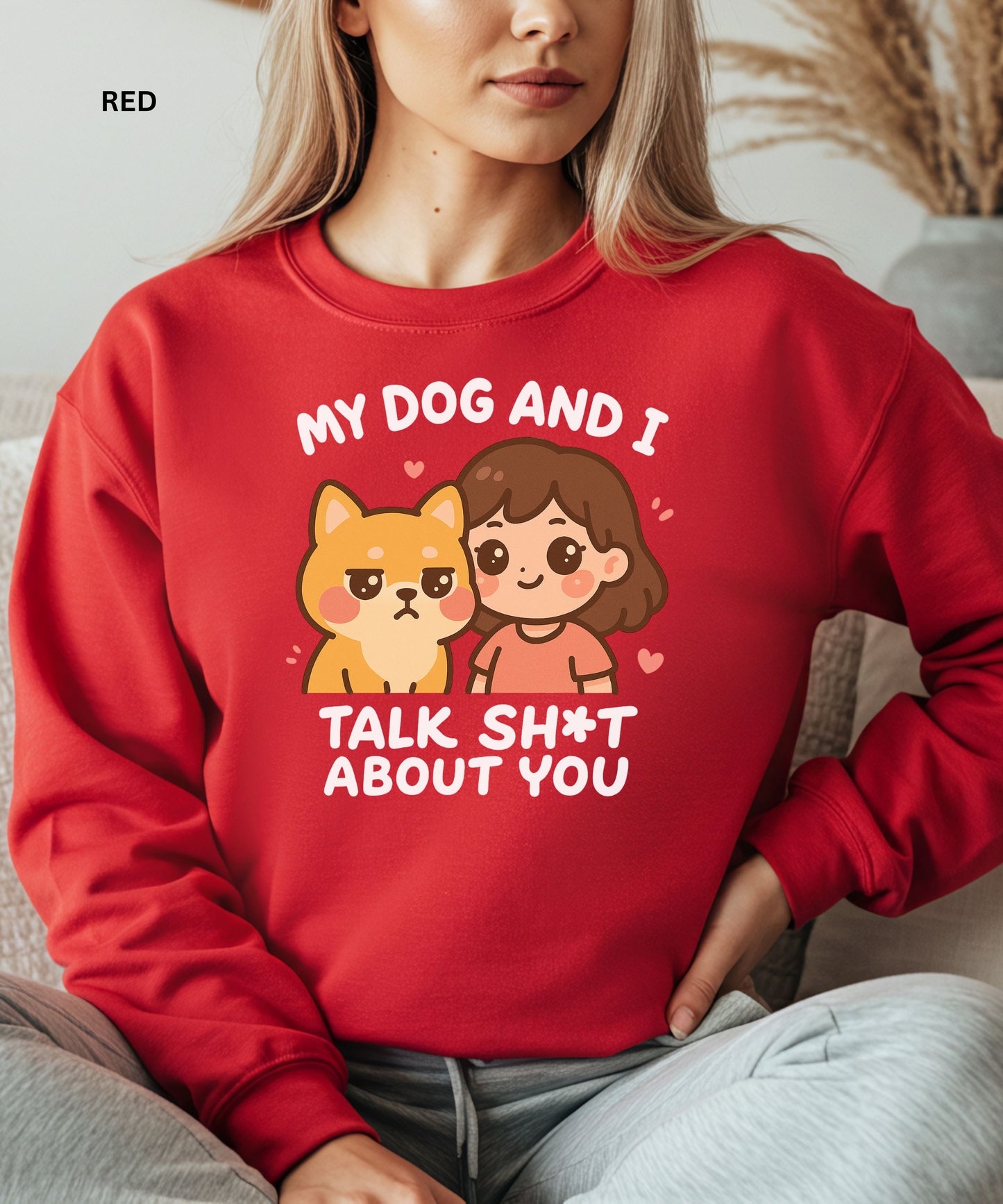Person wearing a red sweatshirt with a graphic and text that says"my dog and i talk shit about you", sitting on a couch.