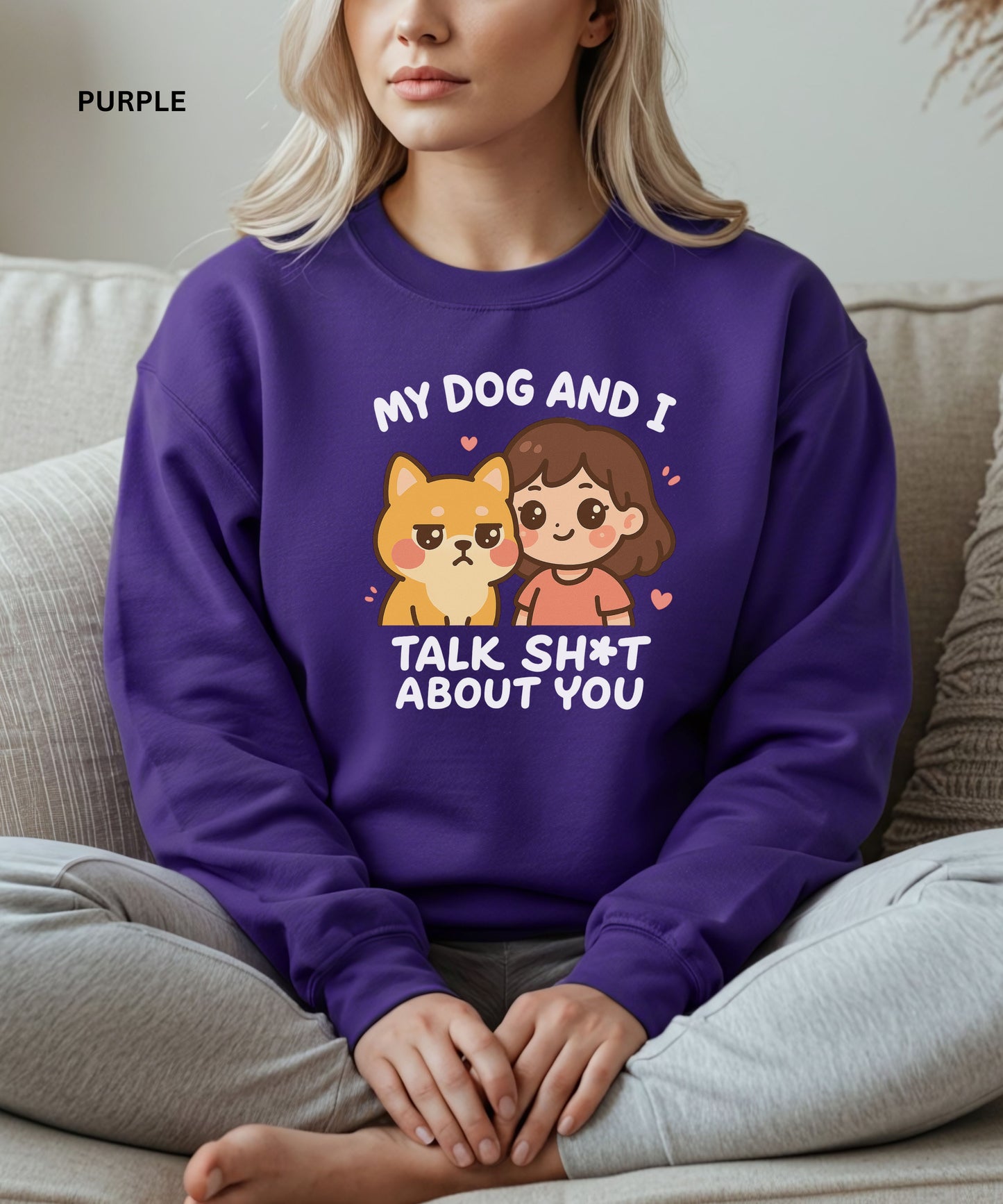 Person wearing a purple sweatshirt with a graphic and text that says"my dog and i talk shit about you", sitting on a couch.