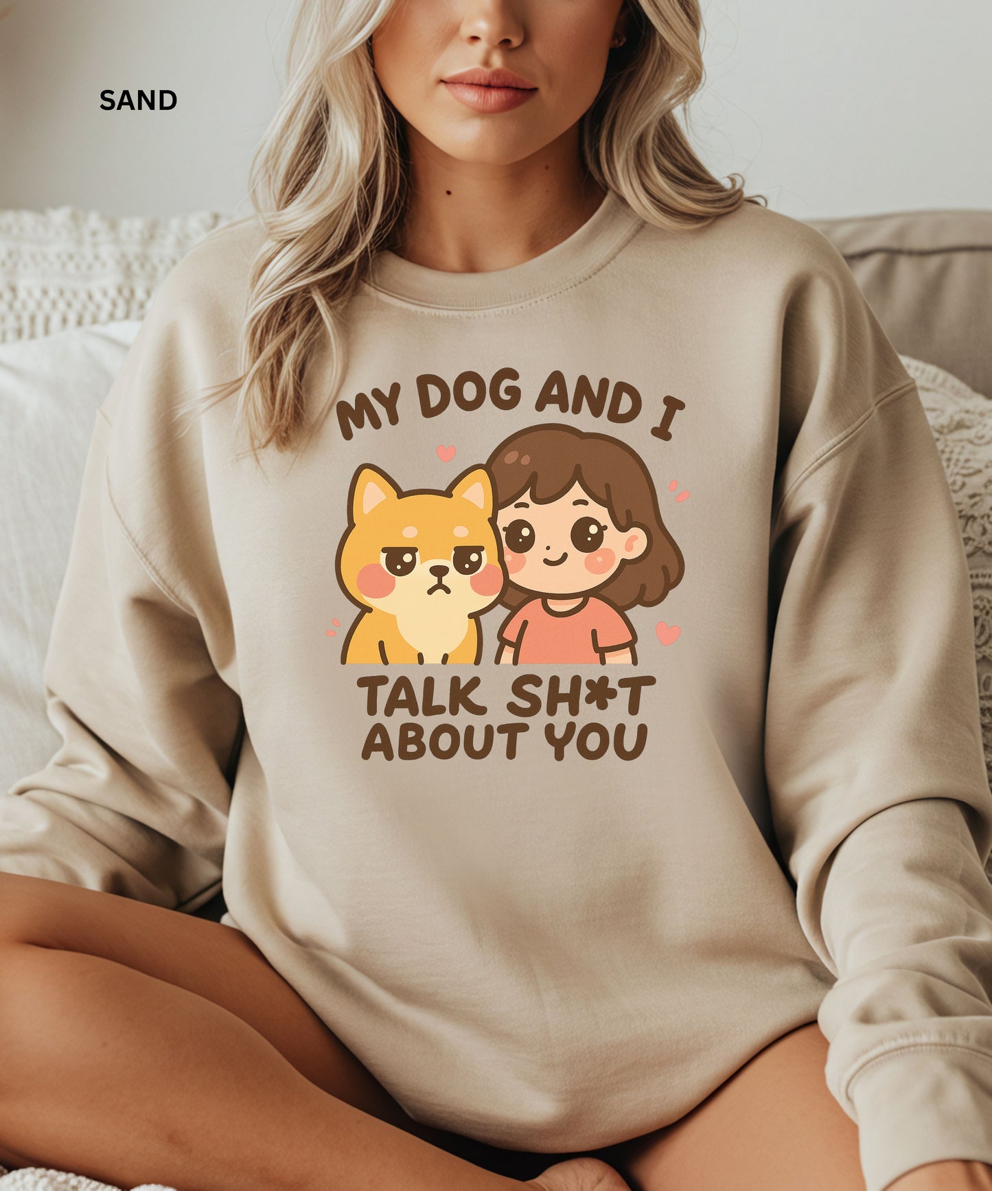 Person wearing a sand sweatshirt with a graphic and text that says"my dog and i talk shit about you", sitting on a couch.