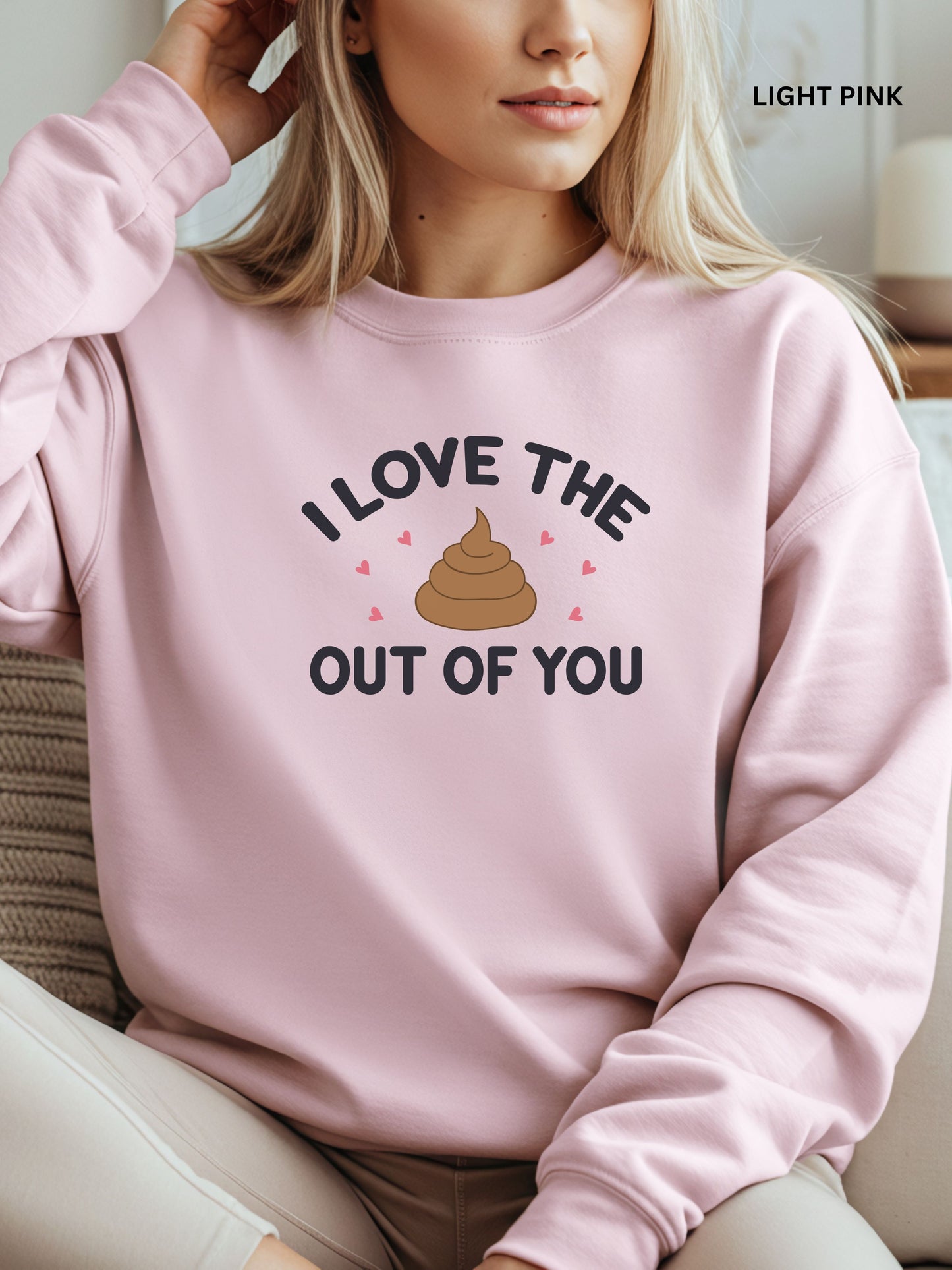Person wearing a light pink sweatshirt with a humorous design that says"i love the shit out of you", sitting on a couch.