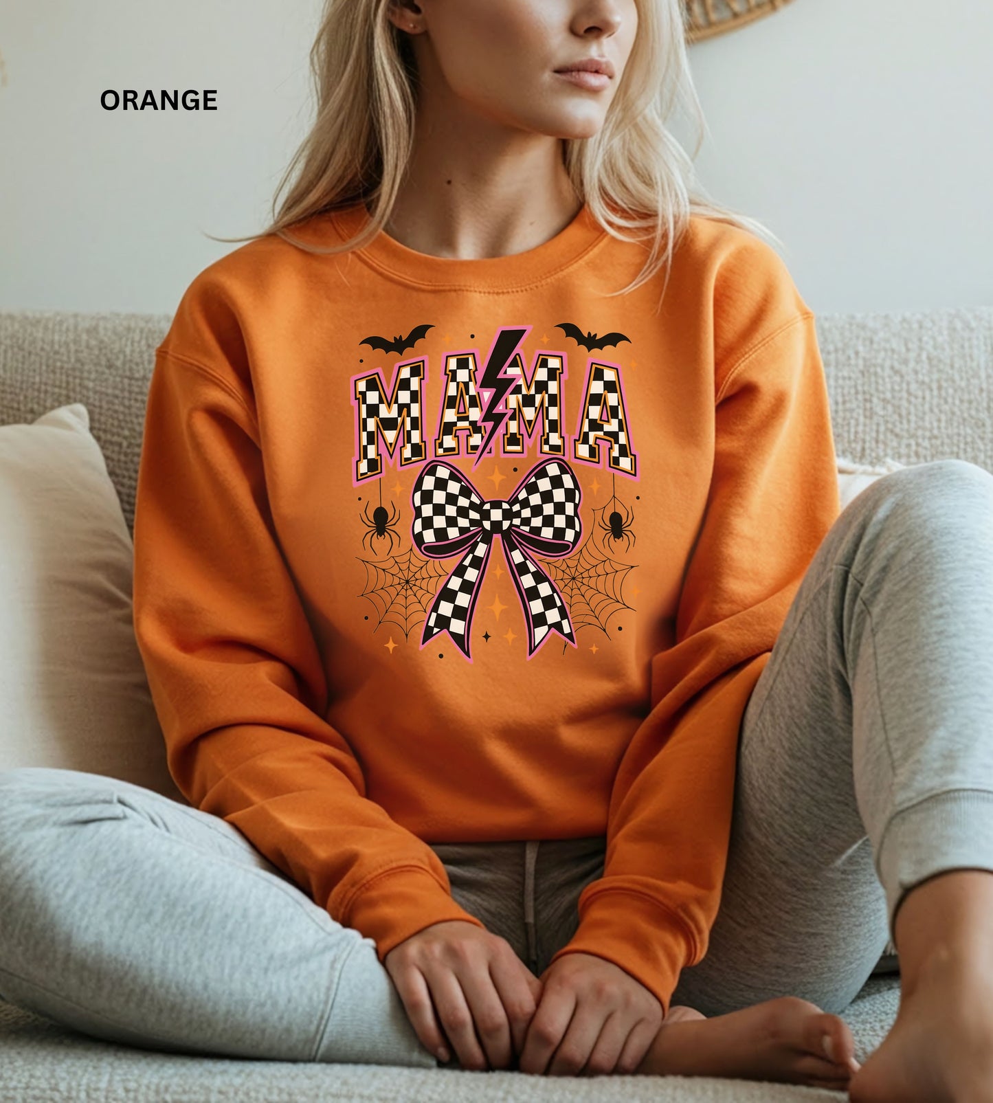 Person wearing an orange sweatshirt with Halloween-themed design " mama" sweatshirt sitting on a couch.