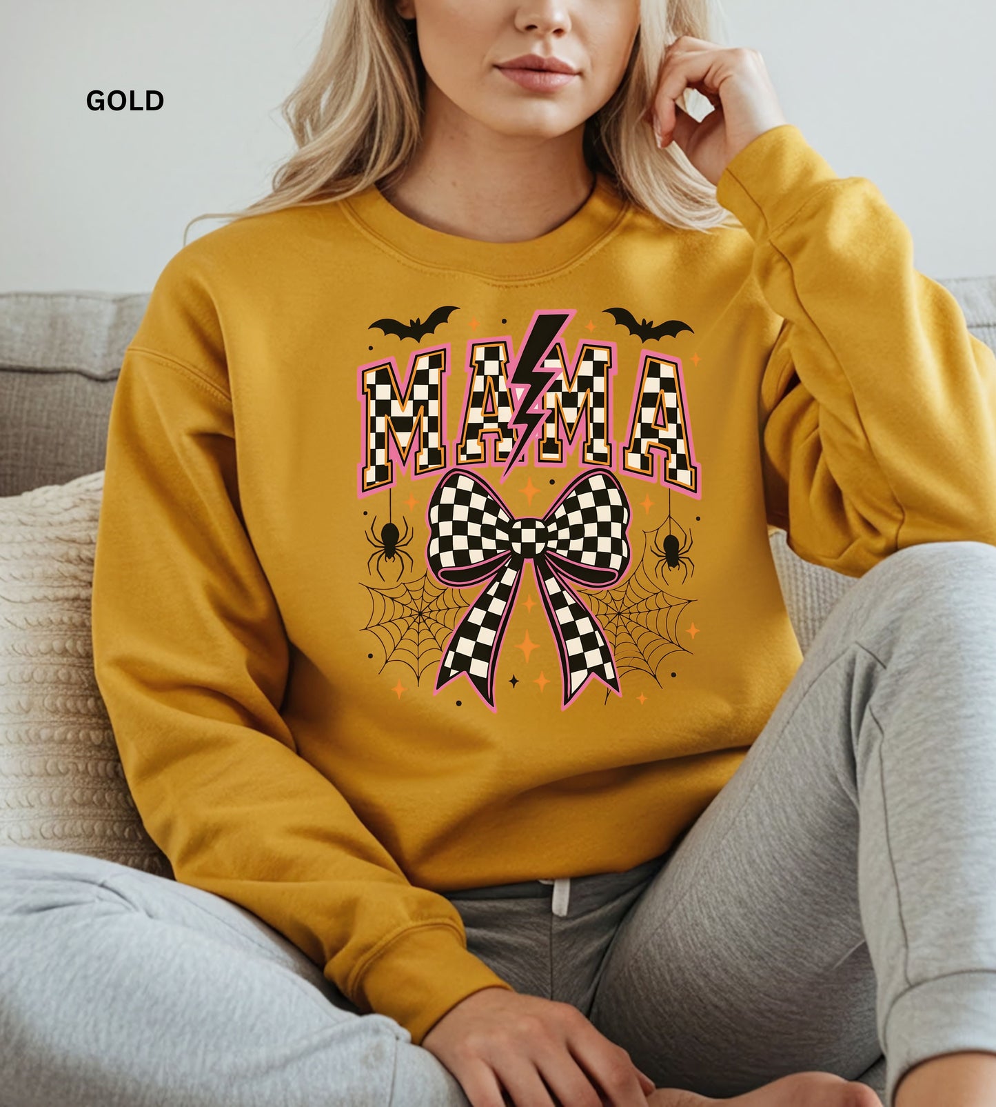 Person wearing a gold sweatshirt with 'MAMA' and bow design, sitting on a couch.