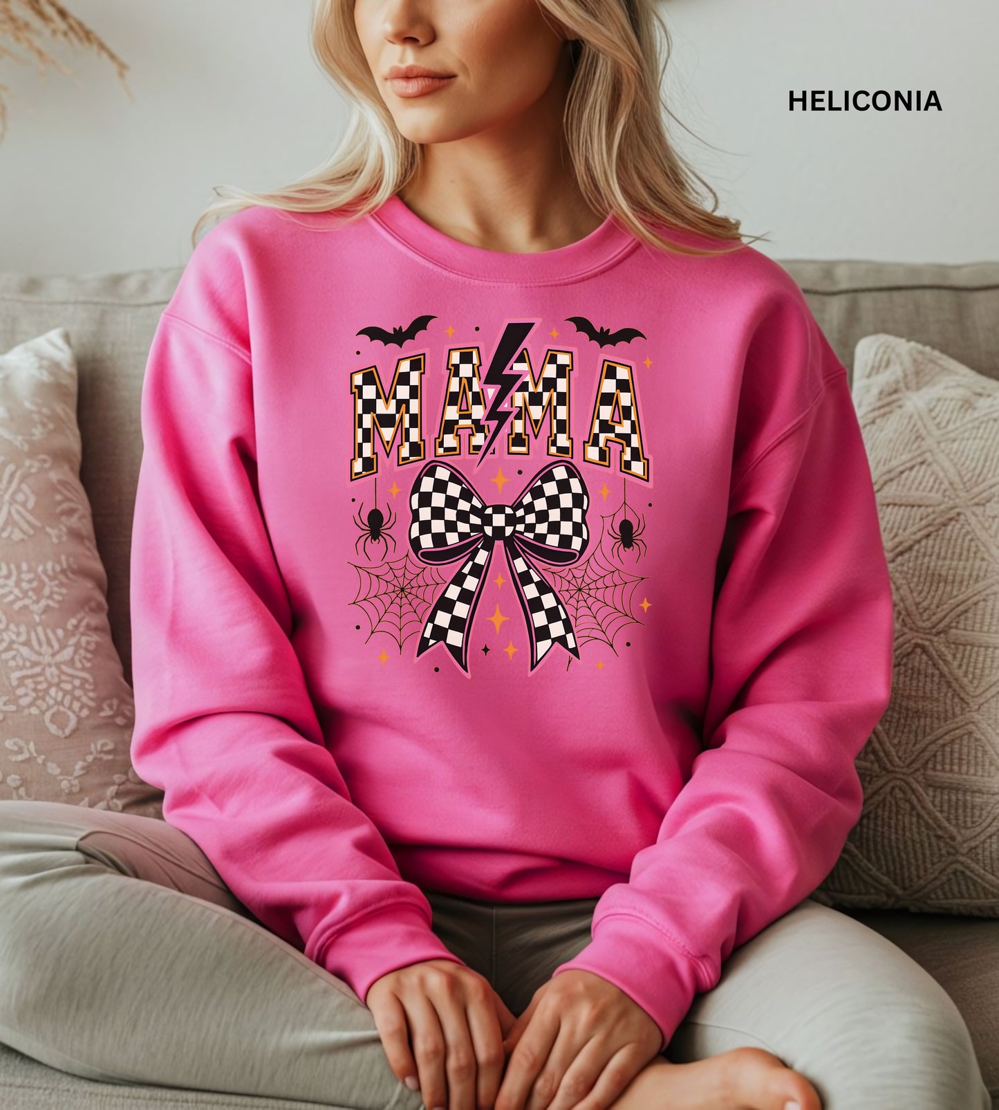Person wearing a heliconia sweatshirt with 'MAMA' and checkered bow design, sitting on a couch.