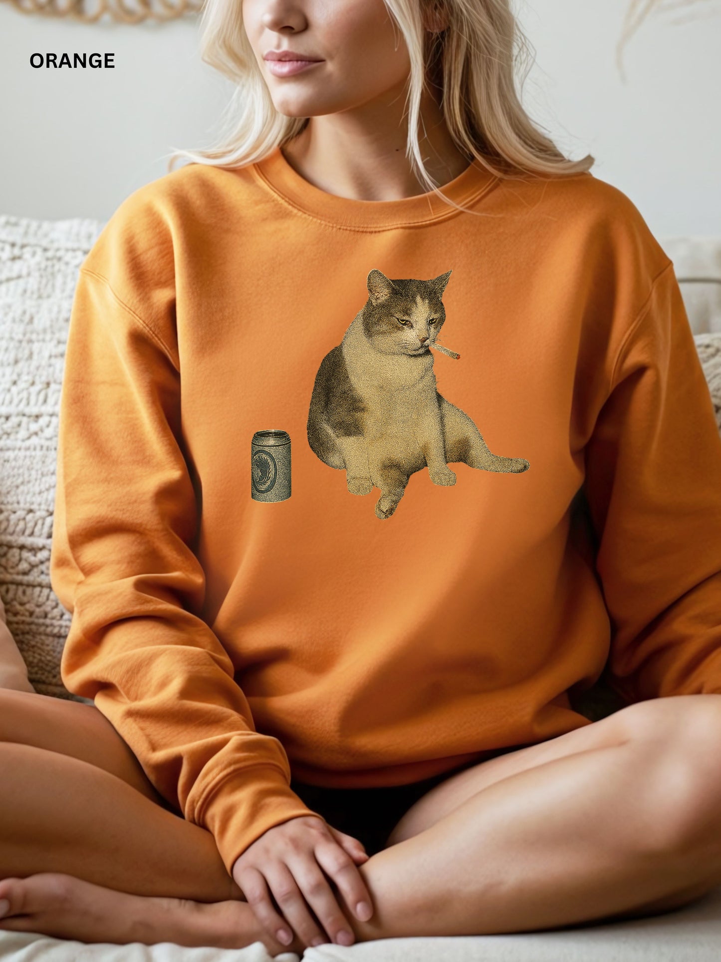 Person wearing an orange sweatshirt with a cat graphic and can design.