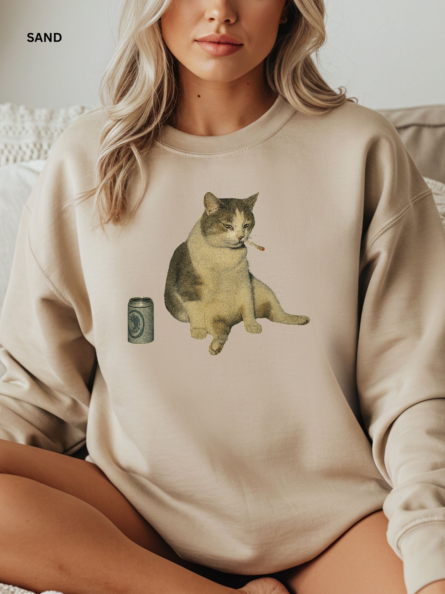 Person wearing a sand sweatshirt with a cat graphic and camera, sitting on a couch.