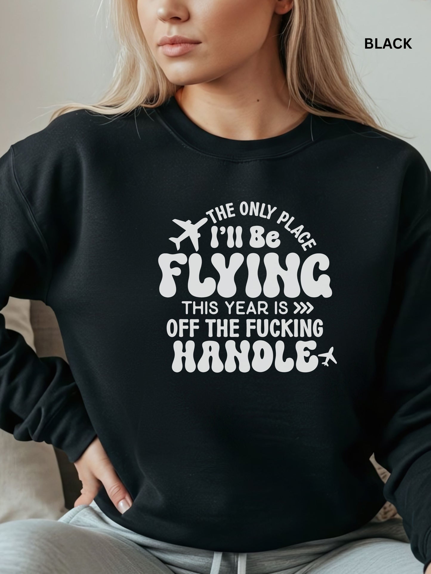 Person wearing a black sweatshirt with a humorous text design that says "the only place ill be flying is off the fucking handle, sitting on a couch.