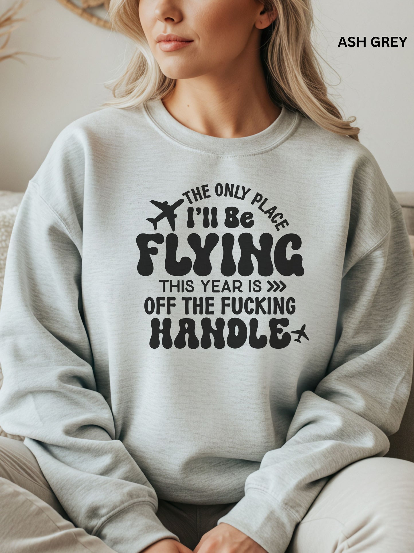 Person wearing an ash grey sweatshirt with a humorous text design that says "the only place ill be flying is off the fucking handle, sitting on a couch.