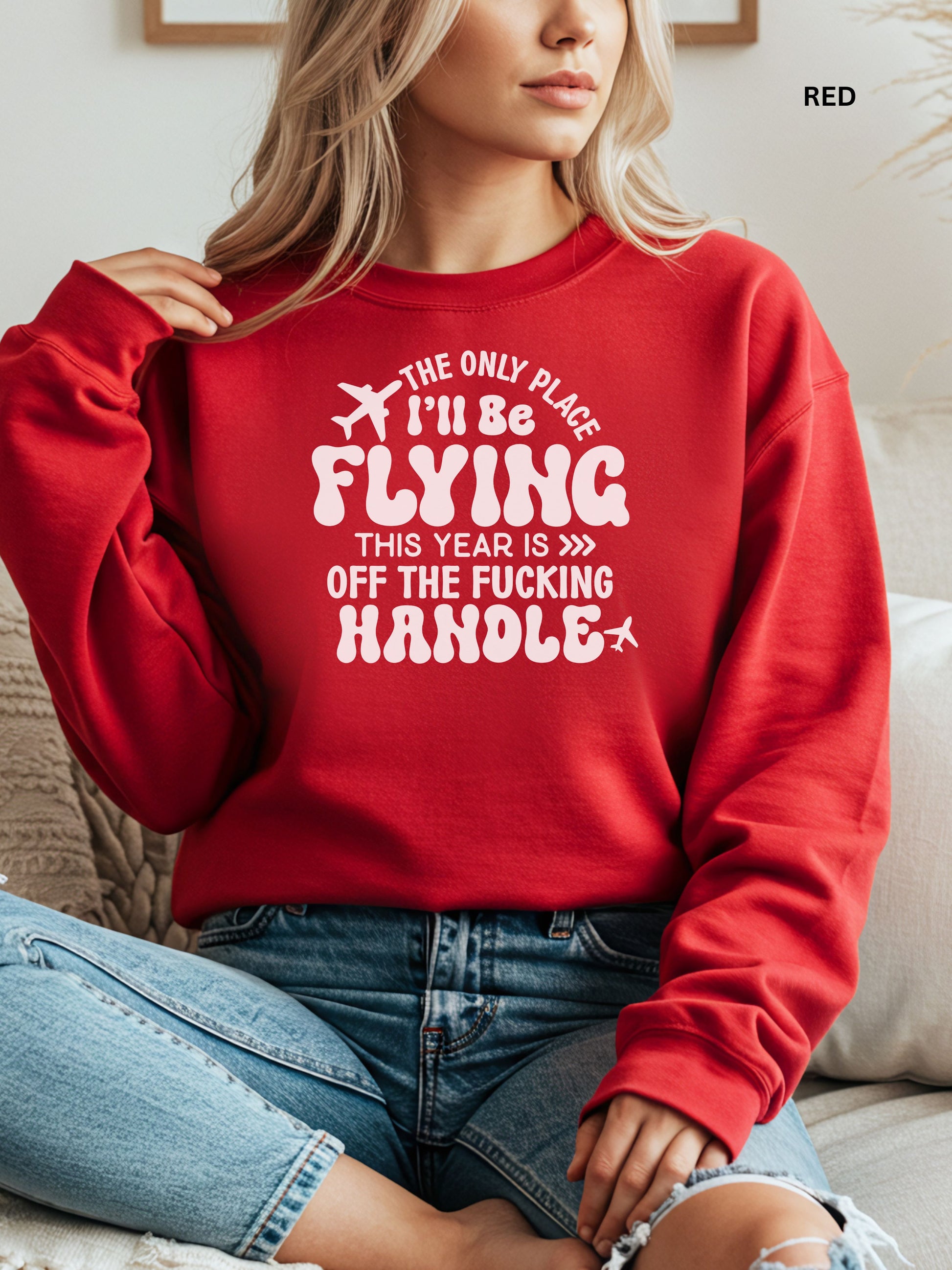 Person wearing a red sweatshirt with a humorous text design that says "the only place ill be flying is off the fucking handle, sitting on a couch.