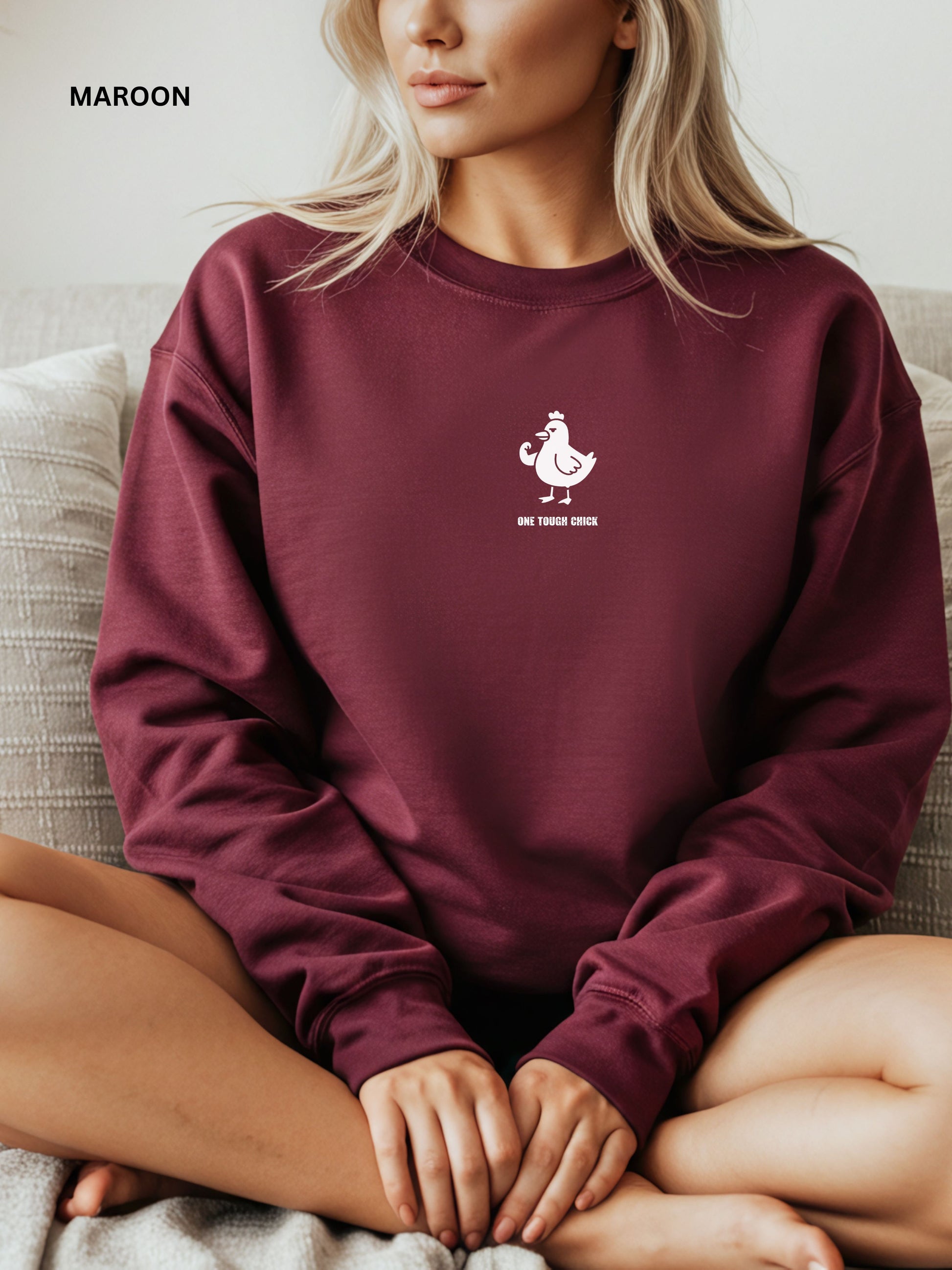 Person wearing a maroon sweatshirt with a logo and text, sitting on a couch.