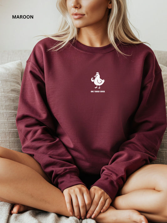 Person wearing a maroon sweatshirt with a logo and text, sitting on a couch.