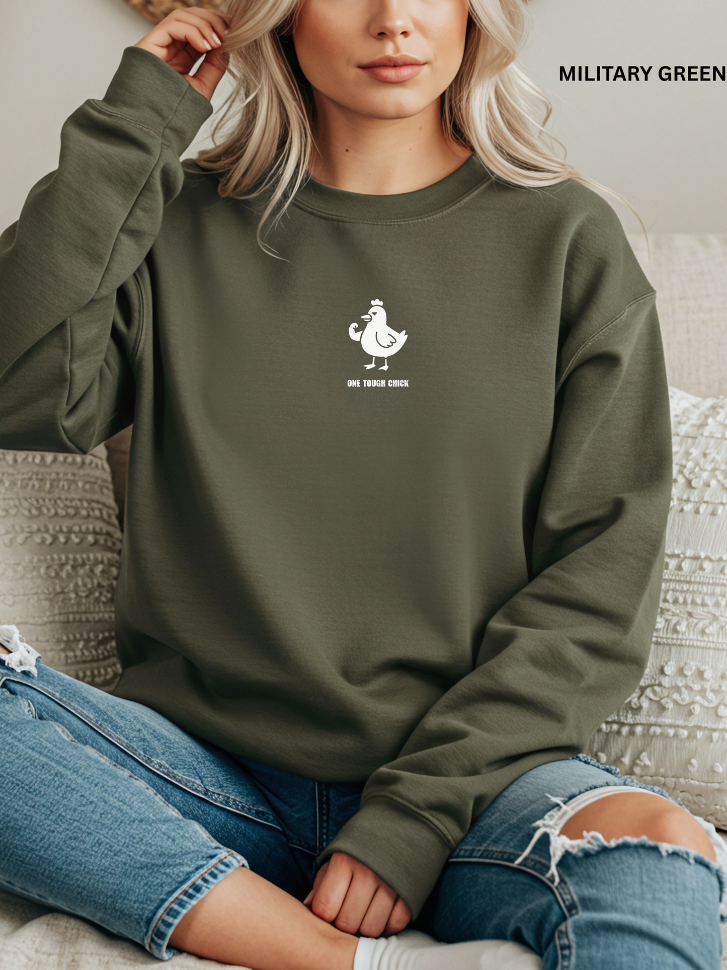 Person wearing a military green sweatshirt with a black logo of a chicken and text " one tough chick", sitting on a textured surface.
