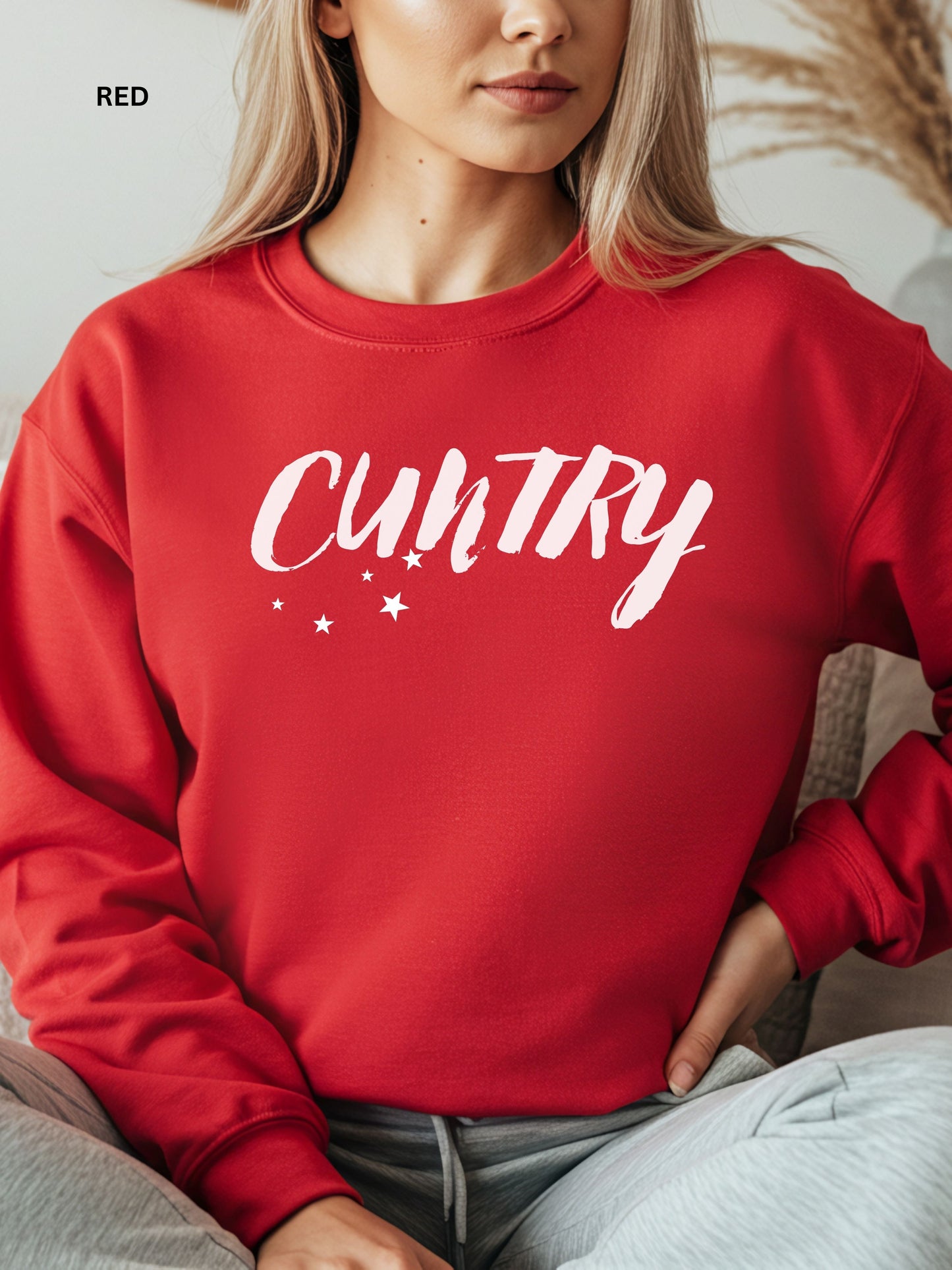 Person wearing a red sweatshirt with 'CUNTRY' printed on it, sitting on a couch.