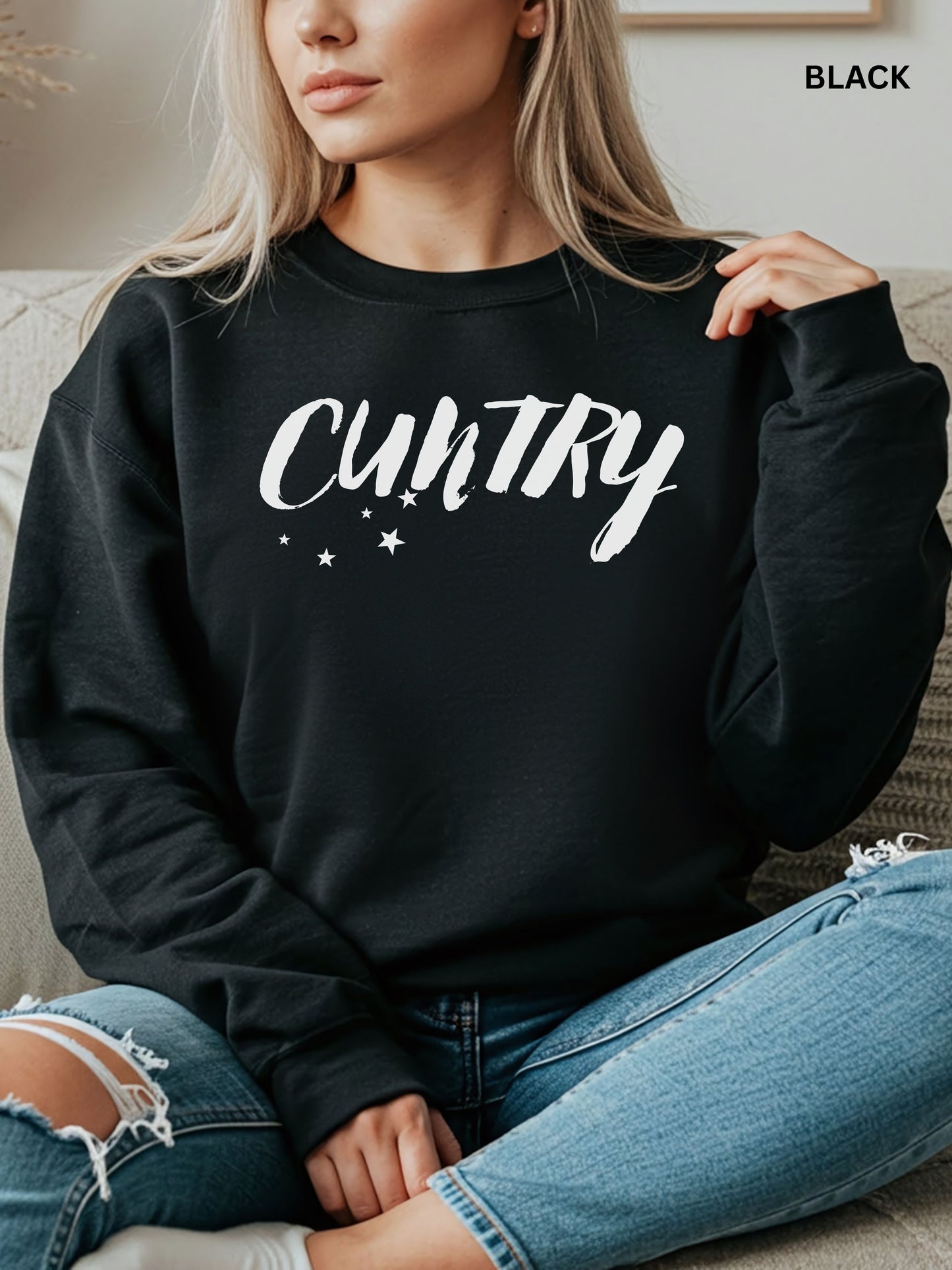 Person wearing a black sweatshirt with 'CUNTRY' printed on it, sitting on a couch.