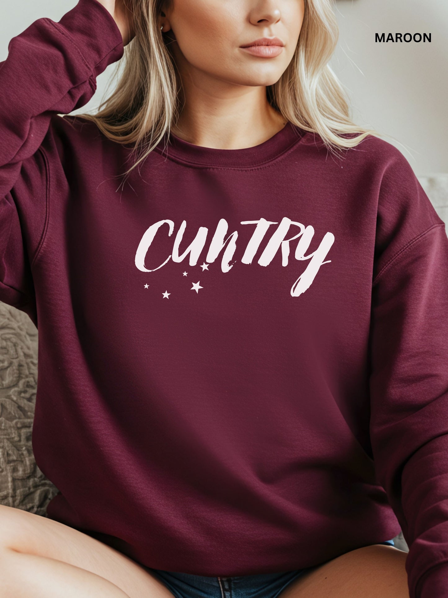 Person wearing a maroon sweatshirt with 'CUNTRY' printed on it, sitting on a couch.