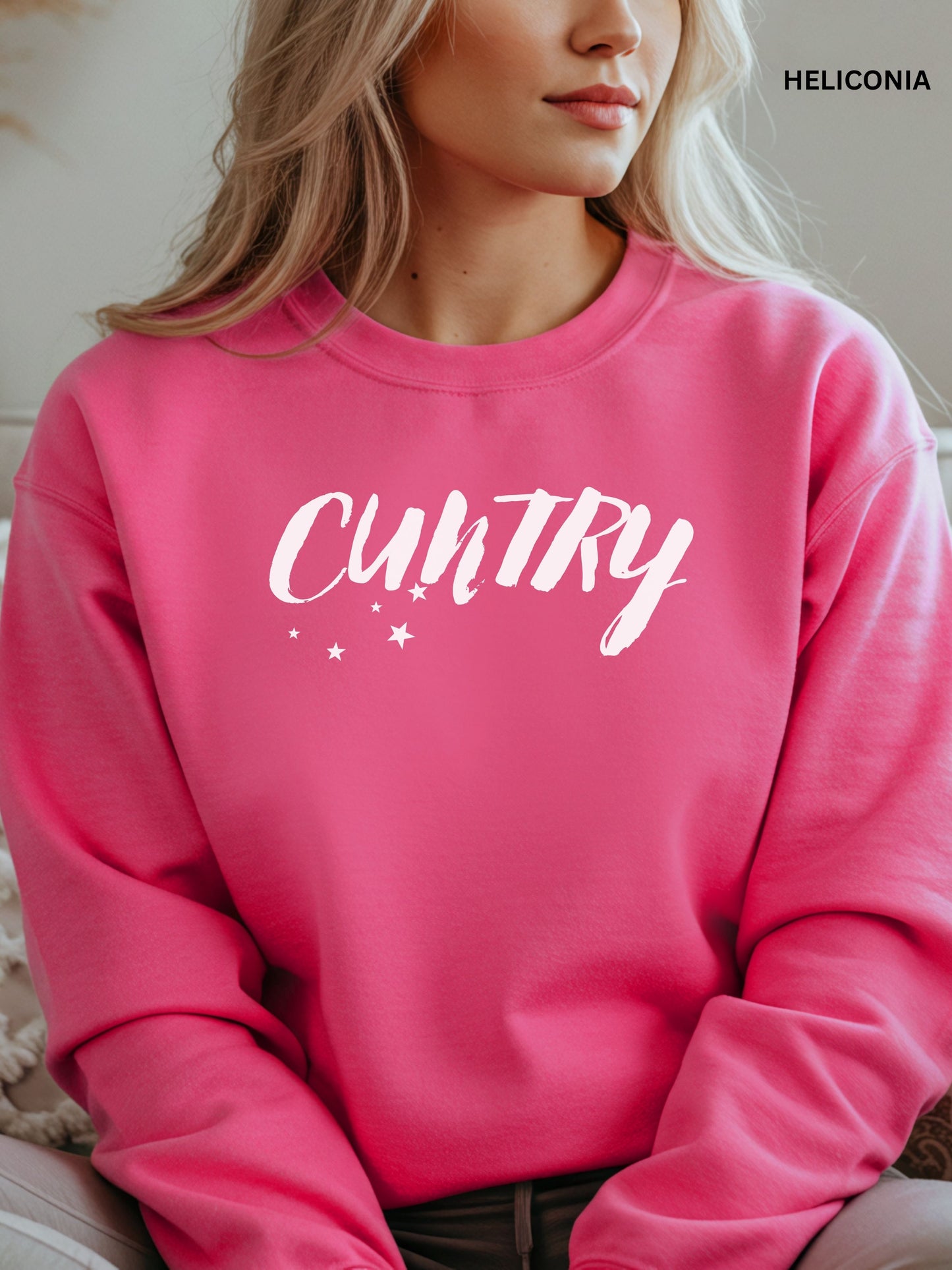 Person wearing a  heliconia sweatshirt with 'CUNTRY' printed on it, sitting on a couch.