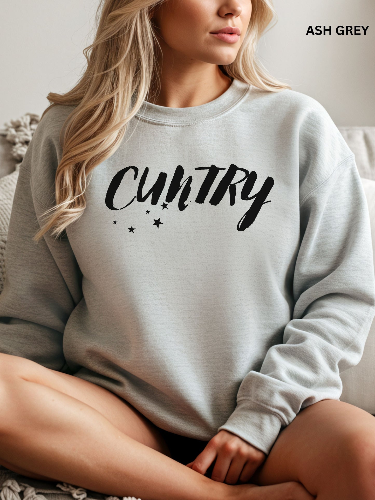 Person wearing an ash grey sweatshirt with 'CUNTRY' printed on it, sitting on a couch.
